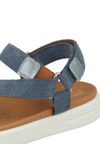 Blaue Wildledersandale mit verstellbaren Riemen und silbernen Akzenten, braunem gepolstertem Fußbett und weißer Gummisohle.