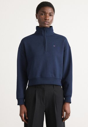 Navy blue pullover sweatshirt with a high collar and half-zip, featuring a ribbed hem and cuffs. Small logo detail on the chest.