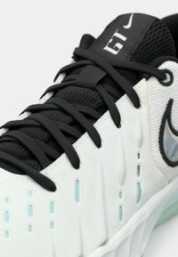 Αθλητικό παπούτσι Nike με μαύρο επάνω μέρος από δίχτυ, λευκό υφή σώμα, κλείσιμο με κορδόνια, αντανακλαστικές λεπτομέρειες και γαλάζιες λεπτομέρειες στα πλευρά.