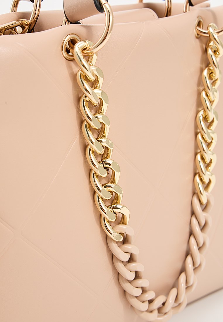 Sac à main rose clair avec une finition texturée, doté de poignées en chaîne métallique dorée et d'un accent en maillons crème épais s'entrelacant avec la chaîne.