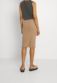 Top court gris et jupe midi côtelée beige, avec une coupe ajustée et une texture. Sandales à semelle plate complètent la tenue.