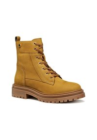 Botas de tobillo de ante marrón con cordones en la parte delantera, cordones marrones y ojales de metal. Suela de goma gruesa con surcos; detalles en el panel lateral.