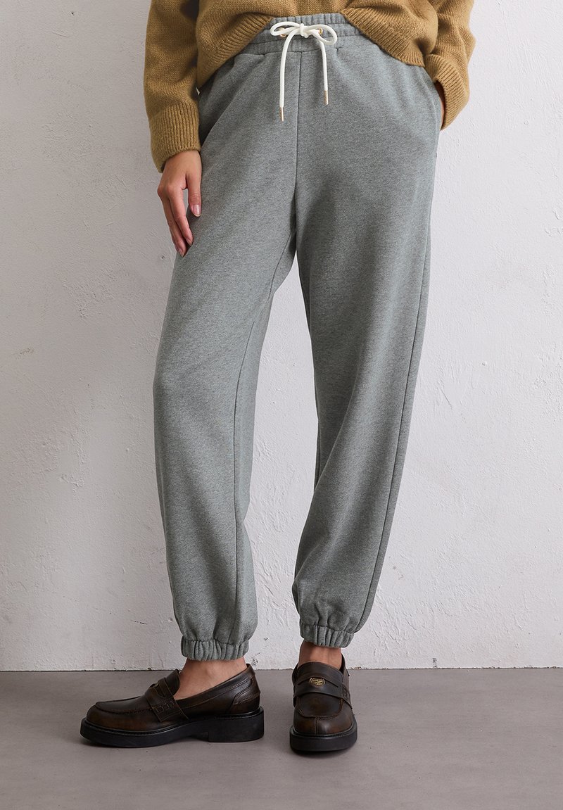 Grijze sweatpants van zacht materiaal, met elastische boorden en een verstelbare tailleband. Gecombineerd met bruine instappers.