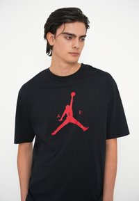 Must t-särk mustast puuvillast, mille ees keskel on suur punane "Jumpman" logo. Ümar kaelus ja lühikesed varrukad, lõdva istuvusega.