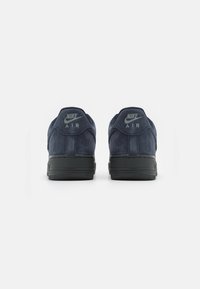 O pereche de adidași Nike Air de culoare albastru închis, văzuți din spate, cu tălpi negre și logo-uri "Nike Air" pe etichetele călcâiului.