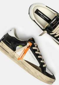 Un paio di sneaker Crime London Skate Deluxe in nero, bianco e beige con lacci beige e un'etichetta arancione sullo sfondo bianco.