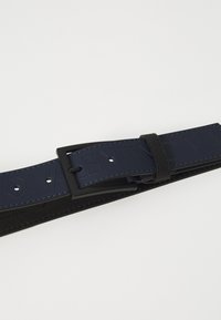 Belt en cuir bleu marine avec un logo en relief, accessoires en métal noir et coutures contrastées. Dispose de plusieurs trous pour un ajustement de taille.