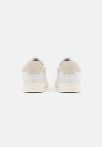 Sneaker bianche in pelle con accenti in suede beige sul tallone e suola in gomma crema, caratterizzate da un design minimale e un branding sottile sul tallone.