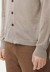 Ljus beige cardigan med en slät textur, med mörka knappar och ribbade manschetter, i kombination med bruna manchesterbyxor.