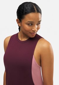 Top sin mangas burdeos con cuello redondo, que presenta un panel en rosa contrastante en el lateral, hecho de un tejido suave y elástico.