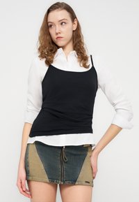 Μαύρο καμησόλ πάνω από λευκό πουκάμισο με κουμπιά, συνδυασμένο με μίνι τζιν φούστα με μπλοκ χρωμάτων σε μπλε και μπεζ και εμπρόσθιο φερμουάρ.