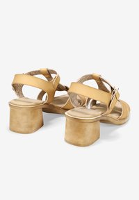 Las sandalias de tacón de cuero amarillo cuentan con correas anchas, una suela texturizada y un robusto tacón cuadrado. El herraje incluye un detalle de hebilla.