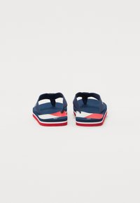 Marine flip-flops med teksturert stropp, med en flerfarget såle i rødt, hvitt og blått. Baksidebilde som fremhever stroppens design.