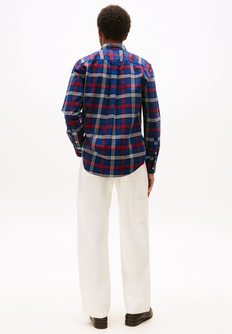 Rutig skjorta i blått, rött och vitt med l�ång ärm och knäppning vid kragen. Bärs med vita vida byxor. Bakvy.