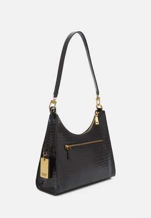 Czarna torebka z tłoczeniem krokodyla, złoty suwak na kieszeni, złote elementy, pasek na ramię oraz zawieszka z logo marki po boku.