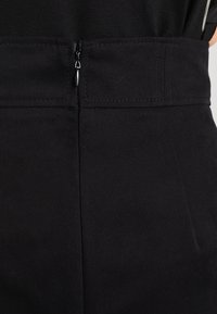 Pantalones negros con un tejido suave y texturizado. Incluyen una cremallera oculta en la cintura y detalles cosidos en las costuras.