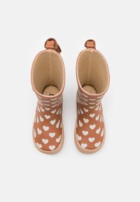 Bottes en caoutchouc marron avec des motifs de cœurs blancs, dotées d'une semelle texturée et d'un intérieur lisse. Comprend une poignée de tirage pour un enfilage facile.