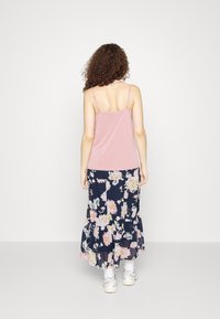 Top de tirantes finos en color rosa, combinado con una falda larga de flores en tonos navy que presenta volantes en capas y patrones florales en rosa y crema.