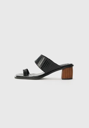 Mustad musta värvi sandaalid, mille ülemine osa on tekstuuriga krokodillimustriga ning puidust ploki kontsaga. Avatud varvastega disain ja lai rihm üle jala.