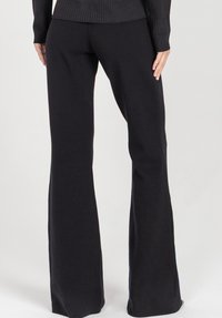Czarne spodnie dzwony wykonane z elastycznego materiału, o gładkiej fakturze i dopasowanej talii, która poszerza się ku dołowi.