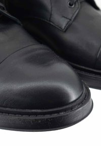 Scarpe in pelle nera con punte arrotondate e dettagli di cucitura. Texture liscia, design minimale, dotate di asole per i lacci e suola piatta.