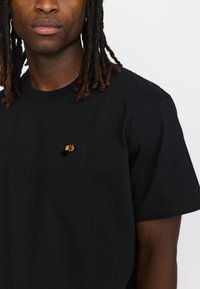 Zwarte katoenen t-shirt met korte mouwen, voorzien van een klein geborduurd geel en blauw ontwerp op de borst, een gladde textuur en een standaard pasvorm.