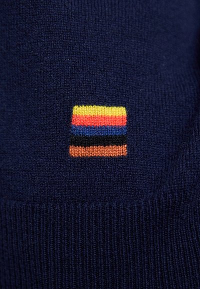 Navy knitted sweater with a small square logo featuring horizontal stripes in yellow, red, blue, black, and orange. Smooth texture.