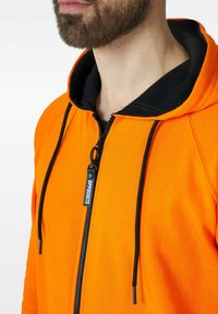 Oranžová mikina na zip s černými akcenty a stahovacími šňůrkami. Má hladký povrch a značkový táhlo zipu, což podtrhuje sportovní design.