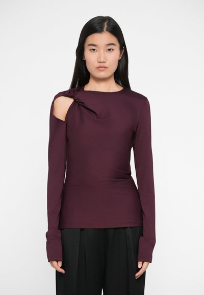 Haut à manches longues, d'un profond bordeaux avec un détail de nœud sur une épaule. Tissu lisse, design ajusté et poignets allongés. Assorti à un pantalon noir.