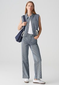 Canotta senza maniche a righe navy e bianche abbinata a pantaloni a vita alta coordinati. La modella indossa un top bianco e tiene una borsa navy. Sneakers bianche.