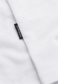 Gros plan sur un tissu en coton blanc avec une petite étiquette tissée noire partiellement visible sur le bord.