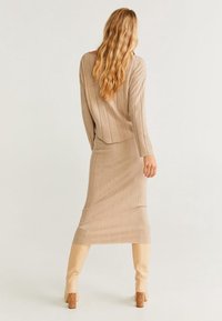 Robe en tricot beige à côtes avec des manches longues, silhouette ajustée et longueur mi-mollet, associée à des bottes hautes beiges, avec un subtil détail de texture.