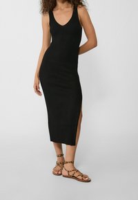 Robe midi noire côtelée avec un décolleté en V profond et des fentes sur les côtés. Associée à des sandales marron avec un imprimé léopard et des brides croisées.