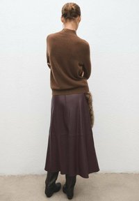 Un pull en cachemire marron associé à une longue jupe en cuir bordeaux foncé avec un accent en fausse fourrure sur le côté.