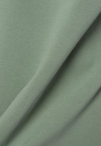 Getextureerde groene stof met een zachte, geweven uitstraling, die een subtiel geribbeld patroon en een zachte draping vertoont.