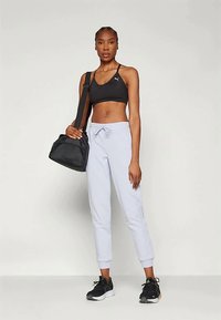 Melnas sporta krūšturis, gaiši pelēki džinsi ar auklu josta, un melni skriešanas apavi. Melna soma ir pārkarināta pār plecu.