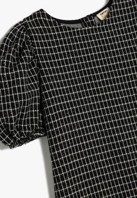 Svart klänning med vitt rutm�önster, med puffärm och rund halslinning, tillverkad av texturerat tyg. Accenterad med små metalltrådar.
