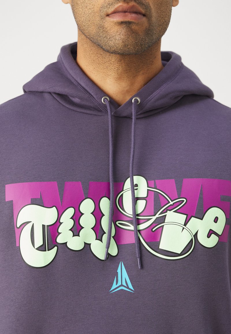 Fioletowa bluza z kapturem z sznurkiem, z dużym różowym i zielonym graficznym napisem. W dolnej części widoczny charakterystyczny niebieski trójkątny logo. Gładka tekstura.