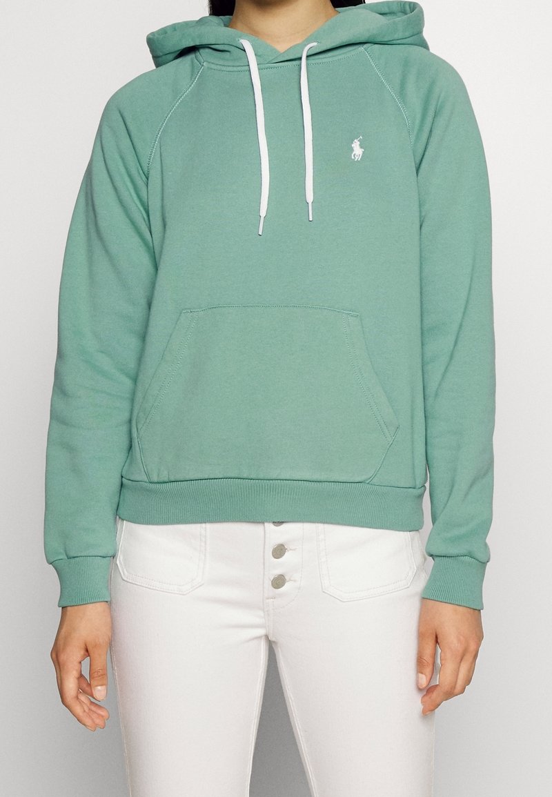 Sudadera con capucha verde en material suave, con un bolsillo frontal, cordones blancos y un pequeño logo en el lado izquierdo del pecho.
