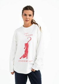Witte sweatshirt met lange mouwen met een rode gestippelde kattenafbeelding en de tekst "IK BEN ELEGANT" en "IK BEN ZO ZO HEEL ELEGANT" in het rood.