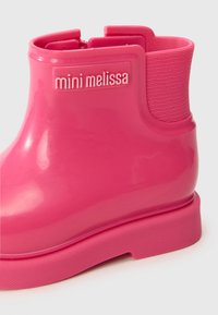 Pink rubber ankle boot with a smooth glossy finish, textured side panel, and a raised logo on the heel area. Flat sole for stability.