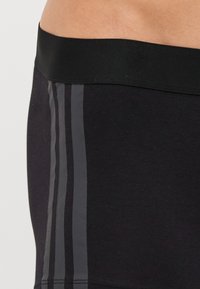 Schwarze Sportshorts mit einem breiten, schwarzen elastischen Bund und zwei vertikalen, dunkelgrauen Streifen an den Seiten. Glatte Textur.