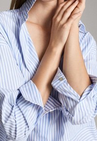 Blauwe en witte gestreepte overhemD met kraag, met lange mouwen en knoopmanchetten, weergegeven met handen die bij de hals zijn samengevouwen.