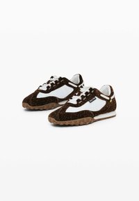 Adidași maro și albaștri cu o textură moale, având un panou lateral alb, sireturi groase și o talpă robustă din cauciuc cu vârfuri.