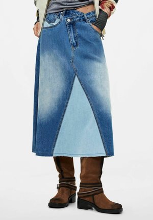 Mujer que lleva una falda midi vaquera de dos tonos con detalle de costura en ángulo y botas marrones de ante hasta la mitad de la pantorrilla con detalles de hebilla.