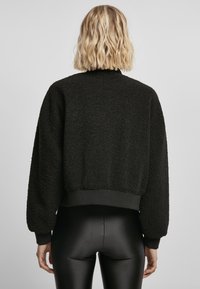 Svart cropped jakke laget av teksturert fleece, med ribbestrikket midje og mansjetter, rund hals og senkehylseslag.