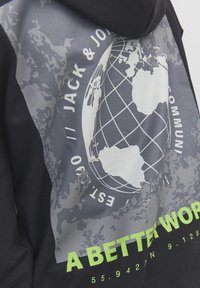 Gros plan sur un hoodie noir et gris avec un graphique de globe, « JACK & JONES », et un texte vert indiquant « UN MONDE MEILLEUR ».