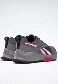 Paire de baskets Reebok grises et noires avec des touches roses et blanches, semelles épaisses et languettes au talon, vues sous un angle arrière latéral.
