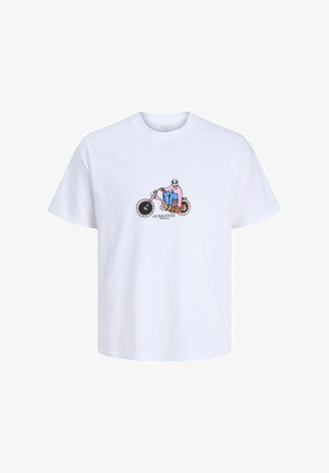 Adolescent garçon aux cheveux bouclés portant une chemise bleu marine déboutonnée sur un t-shirt blanc à motif, un pantalon beige ample et des chaussures en cuir marron, debout et regardant à droite.