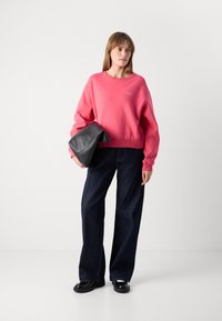 Pink sweatshirt with crew neckline, loose fit, ribbed cuffs, paired with dark denim wide-leg pants and a slouchy black clutch.